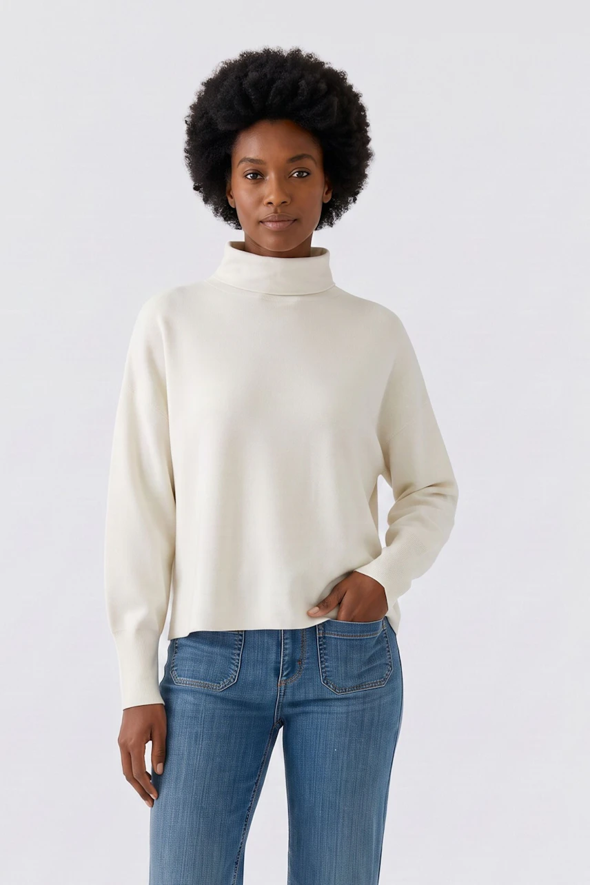 Damen-Pullover: Frau im cremefarbenen Pullover mit Rollkragen und blauer Jeans, lässig und modern.