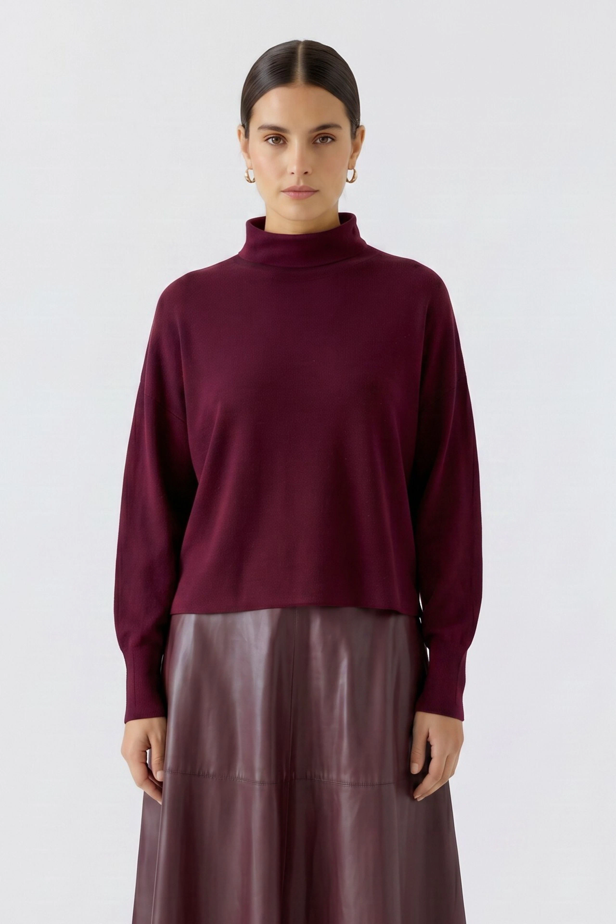 Frau im weinroten Pullover mit Stehkragen, kombiniert mit einem Rock. Schlichtes, modernes Design.