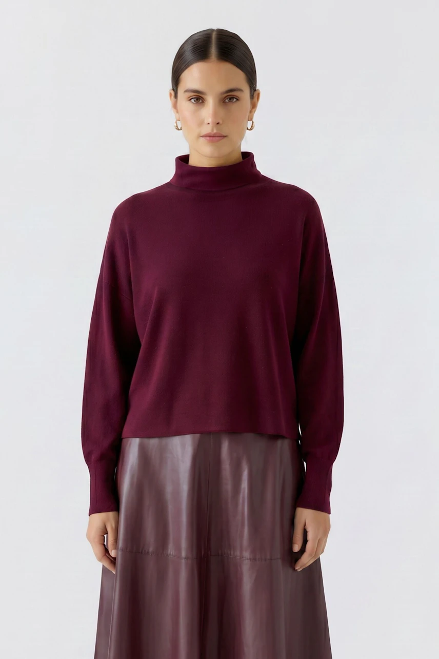 Frau im weinroten Pullover mit Stehkragen, kombiniert mit einem Rock. Schlichtes, modernes Design.