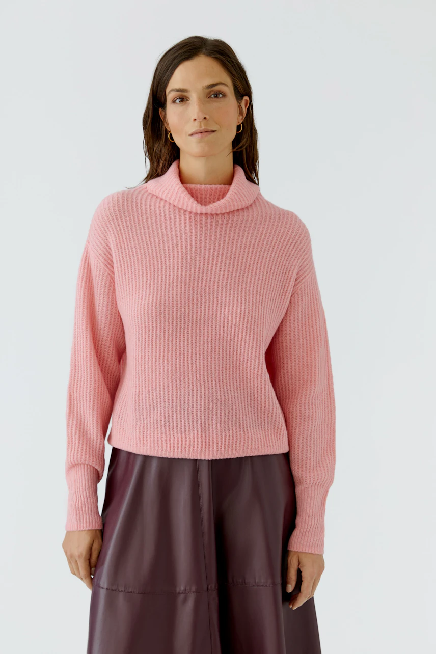 Frau im rosa Pullover: Lockerer Strickpullover mit Rollkragen, kombiniert mit dunklem Rock.