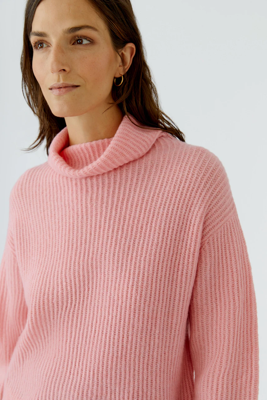 Frau im rosa Pullover mit Rollkragen, lässig und modern, schaut zur Seite.