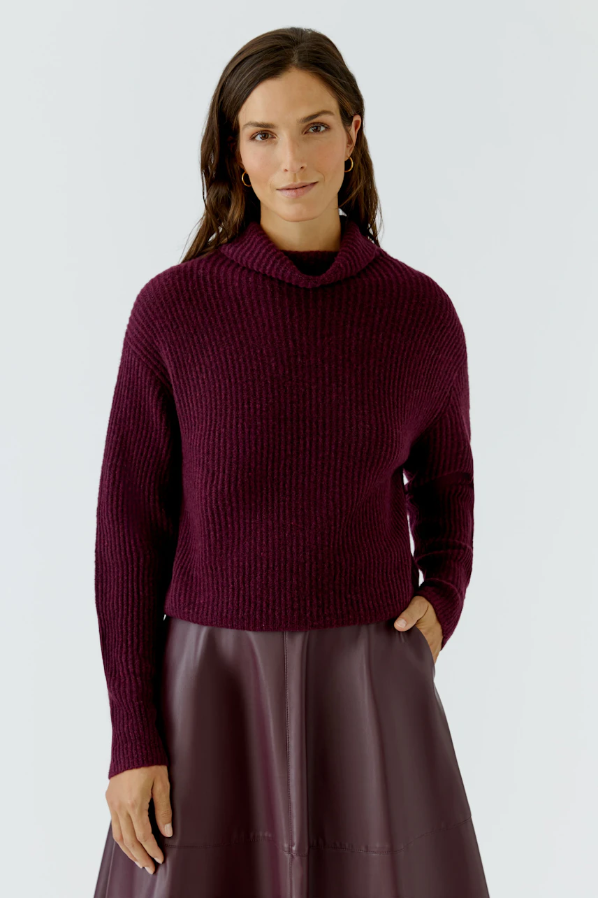 Frau im weinroten Pullover, lässig kombiniert mit Rock. Der Pullover hat einen lockeren Schnitt und Rollkragen.