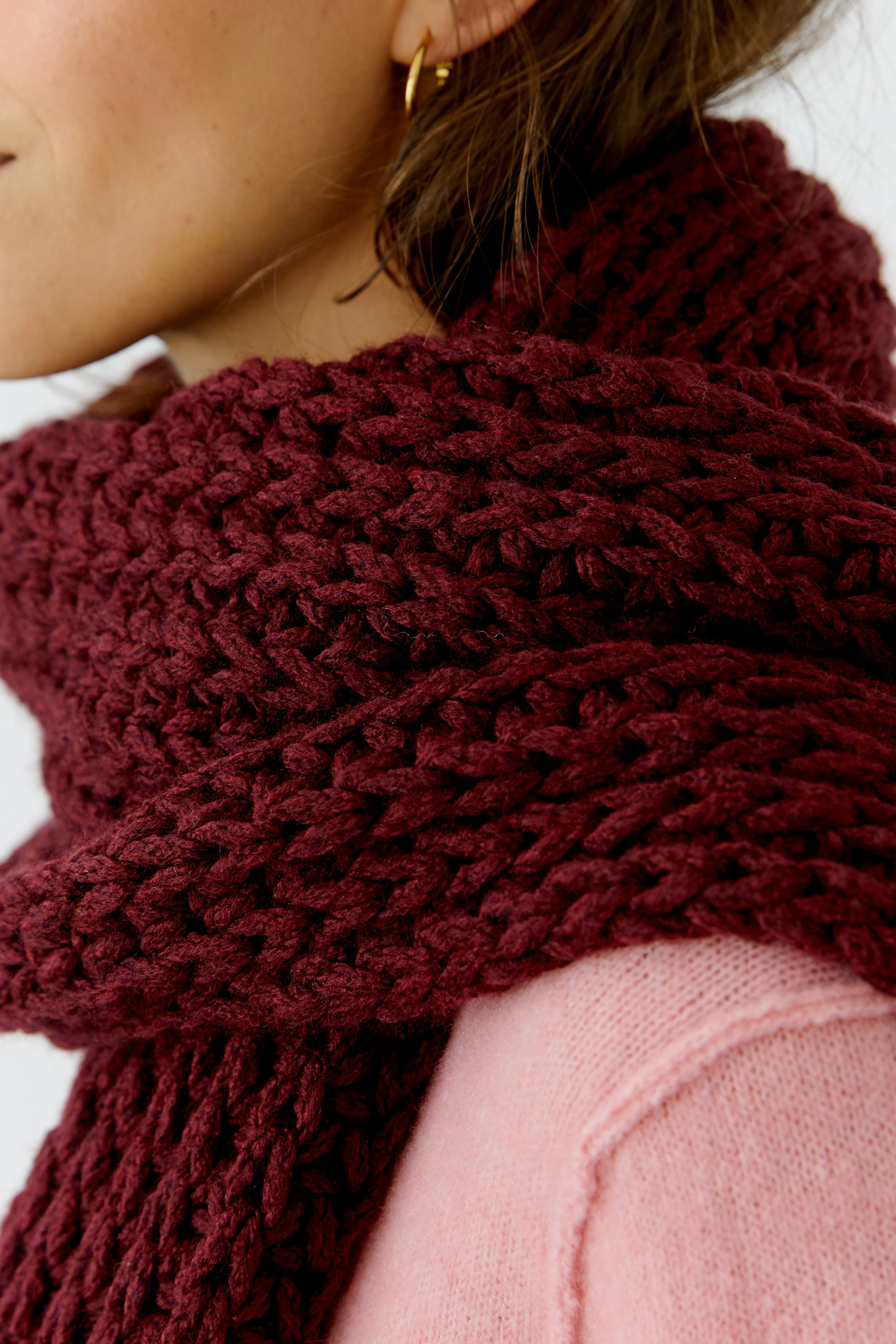 Cozy knit scarf: Woman in a thick, burgundy scarf paired with a soft pink pullover.