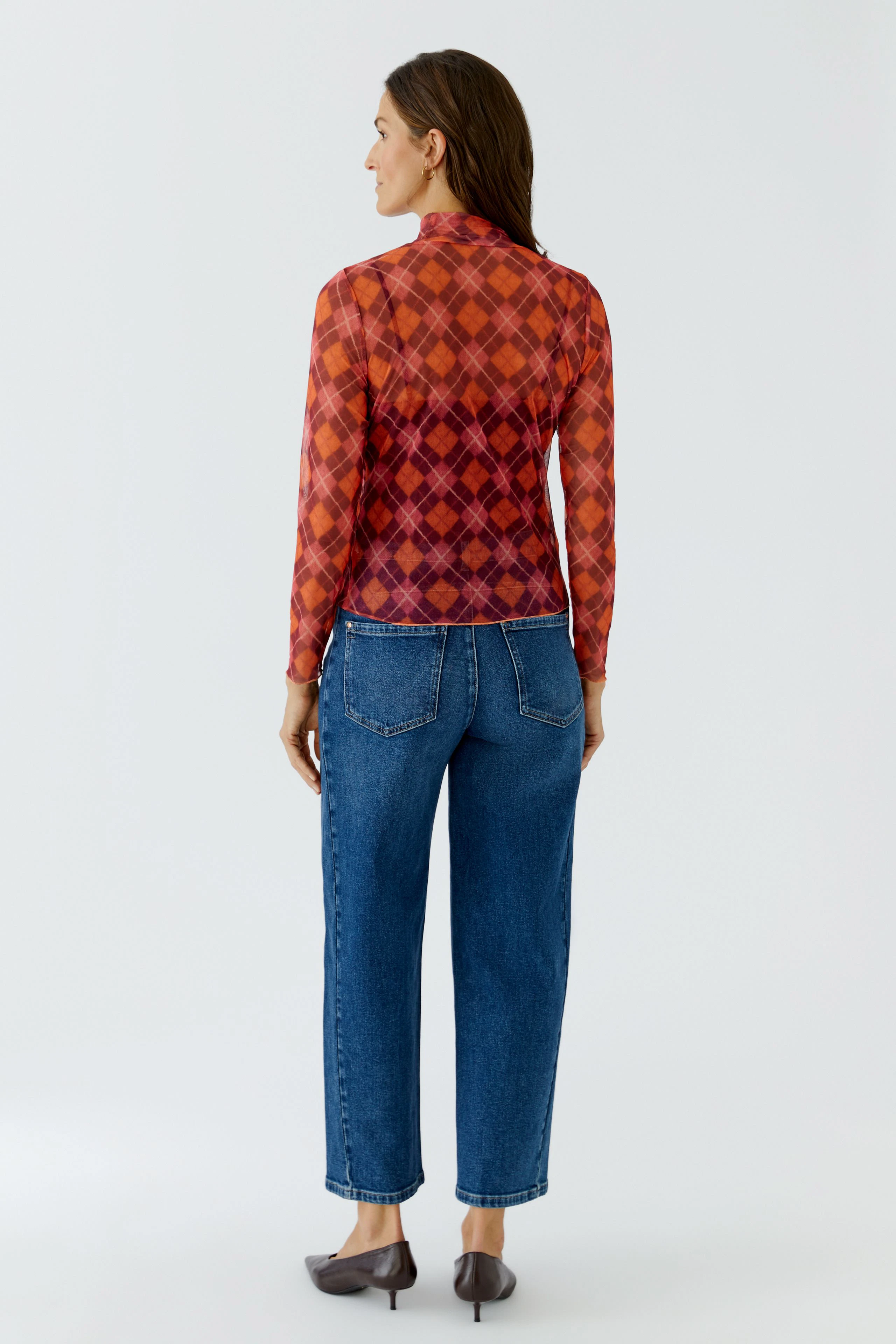Frau im karierten Langarmshirt in Rot-Orange, kombiniert mit blauer Jeans, von hinten gesehen.