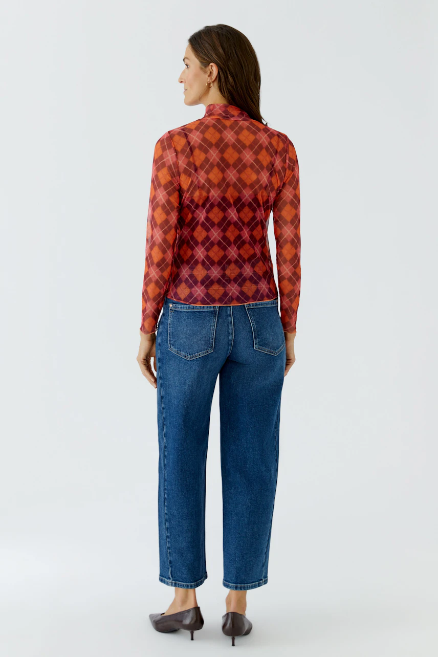 Frau im karierten Langarmshirt in Rot-Orange, kombiniert mit blauer Jeans, von hinten gesehen.