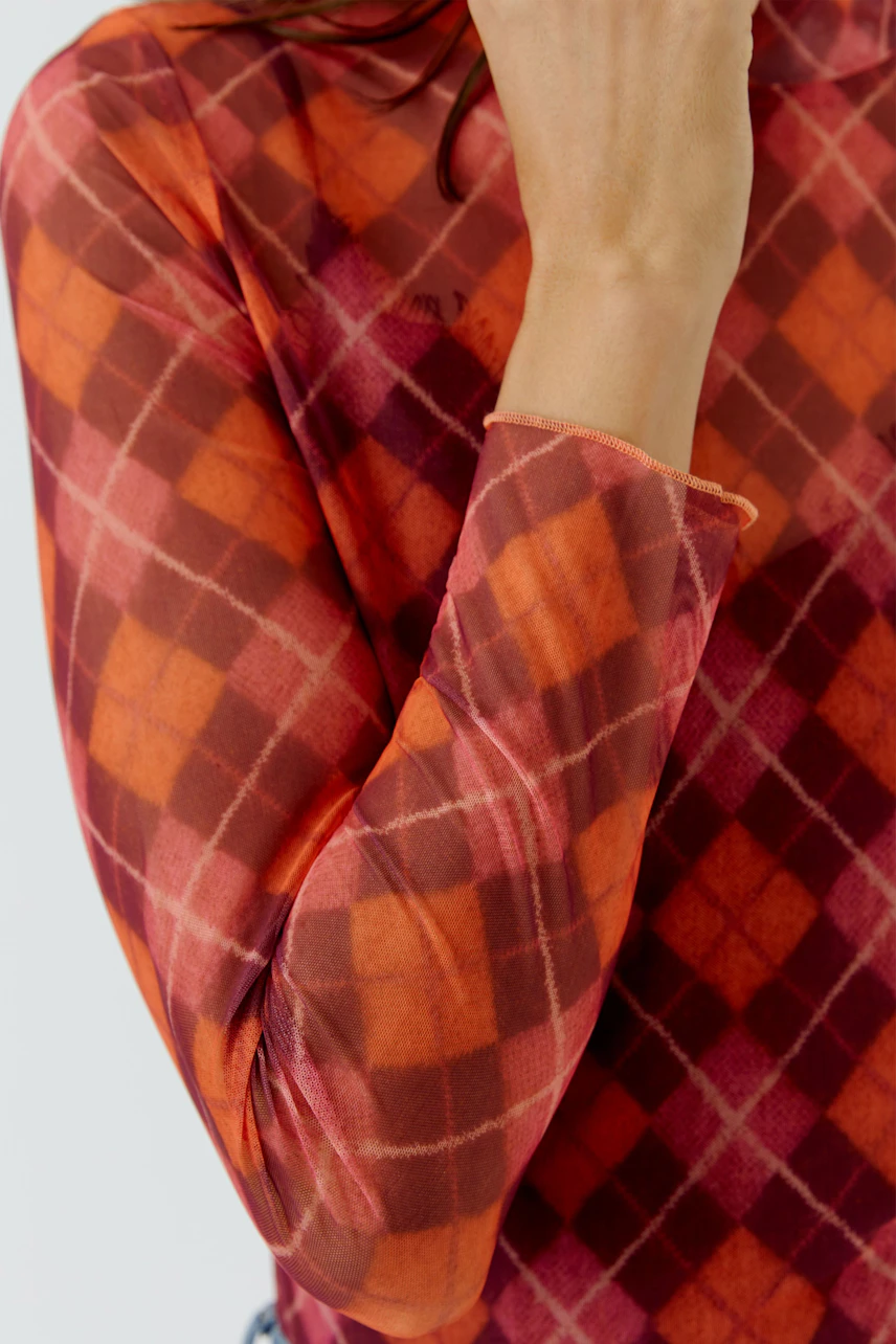 Frau im karierten Langarmshirt in Rot-Orange-Tönen, hält den Kragen, modernes Design.