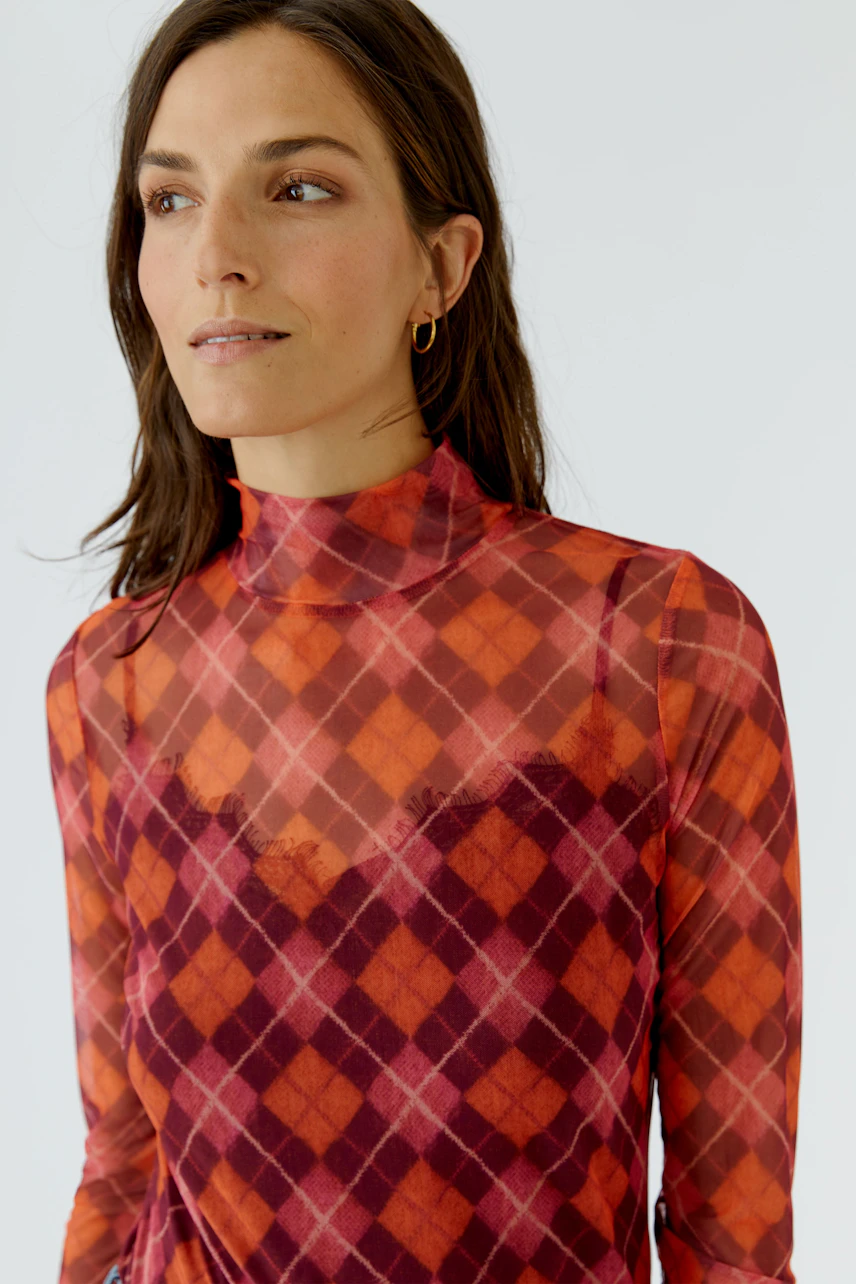 Frau im karierten Langarmshirt in Rot- und Orangetönen, schaut zur Seite. Modisches Design für Damen.