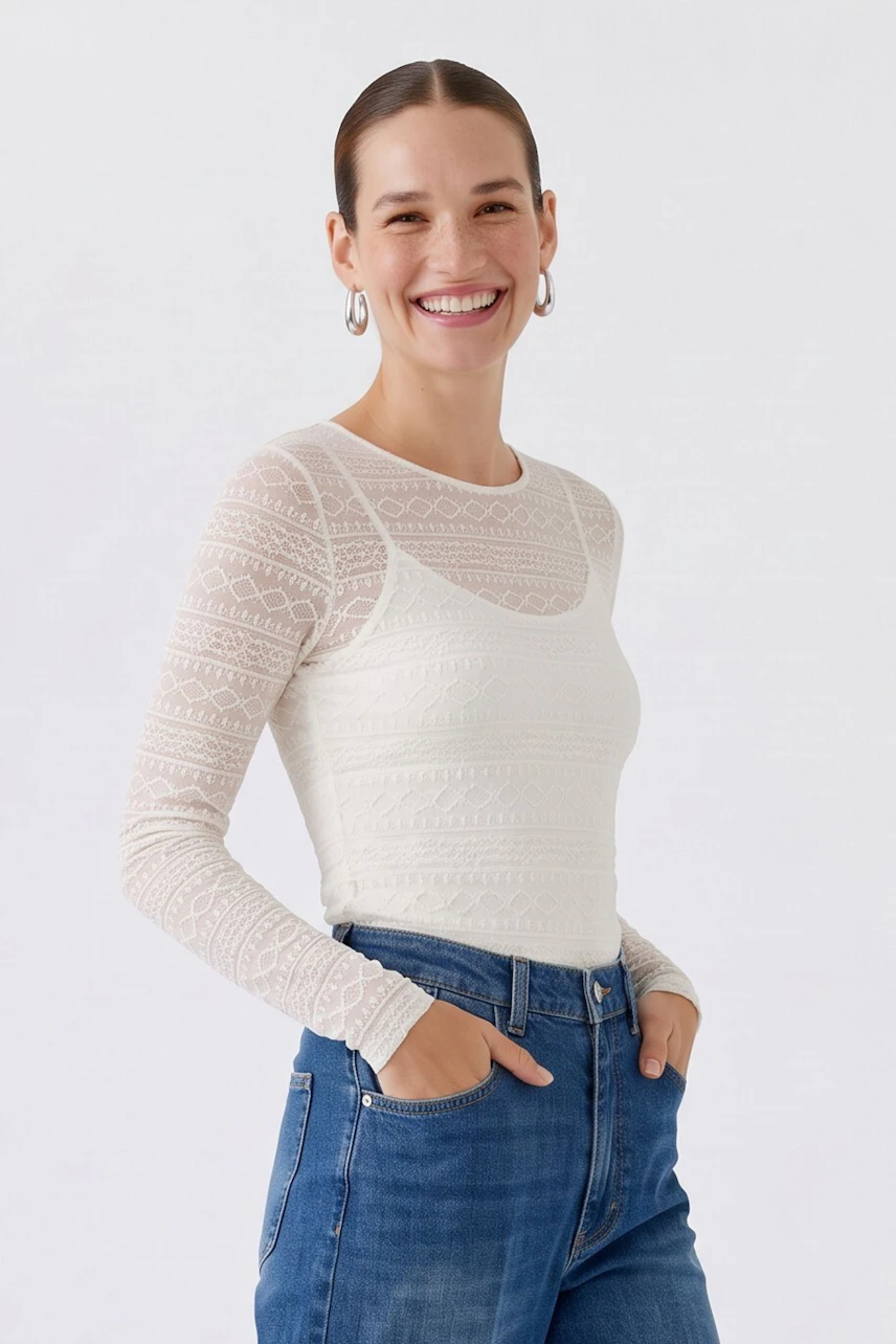 Casual long-sleeve shirt: Woman in a textured white shirt and blue jeans, standing confidently.