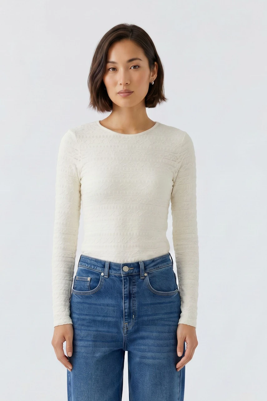 Frau im weißen Langarmshirt und blauer Jeans, schlicht und modern.