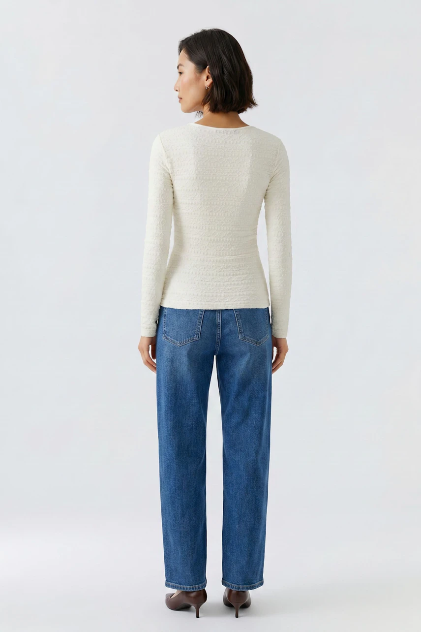 Frau im weißen Langarmshirt und blauer Jeans, von hinten gesehen. Schlichtes Design, ideal für den Alltag.