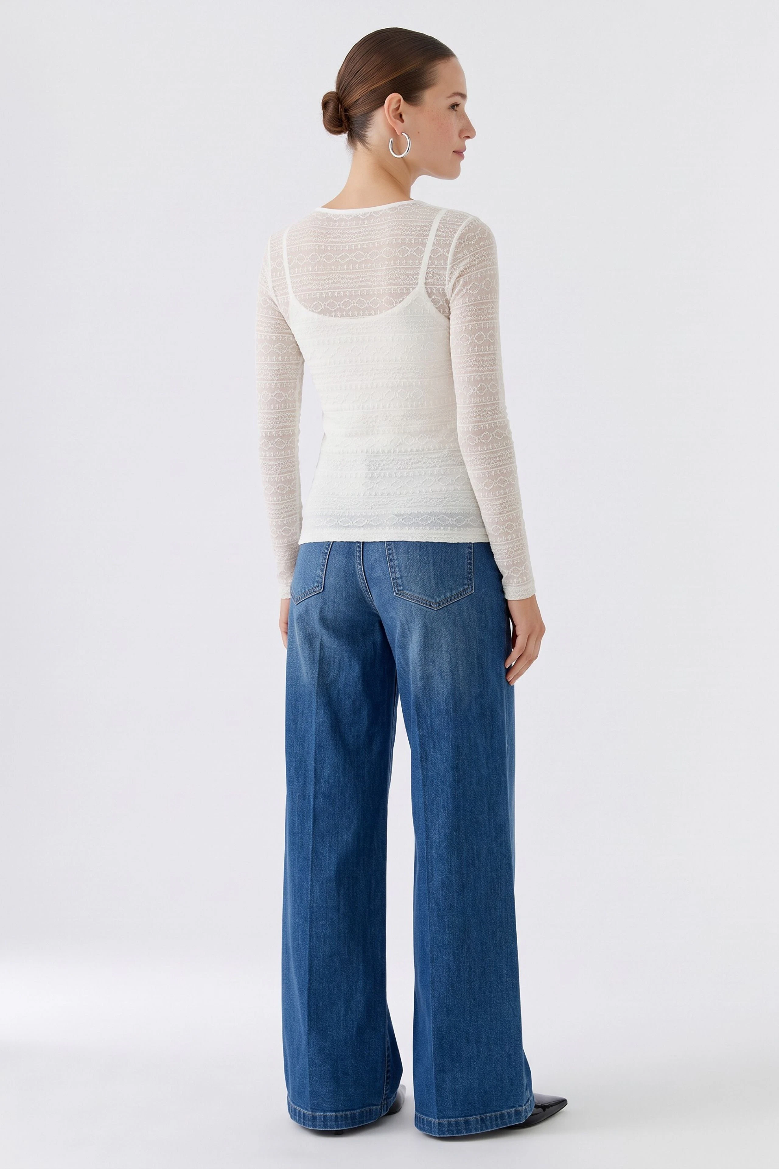 Frau im weißen Langarmshirt und blauer Jeans, von hinten gesehen. Schlichtes Design, ideal für den Alltag.