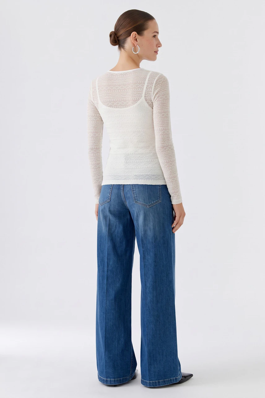 Casual long-sleeve shirt: Woman in a white textured shirt and blue jeans, standing confidently.