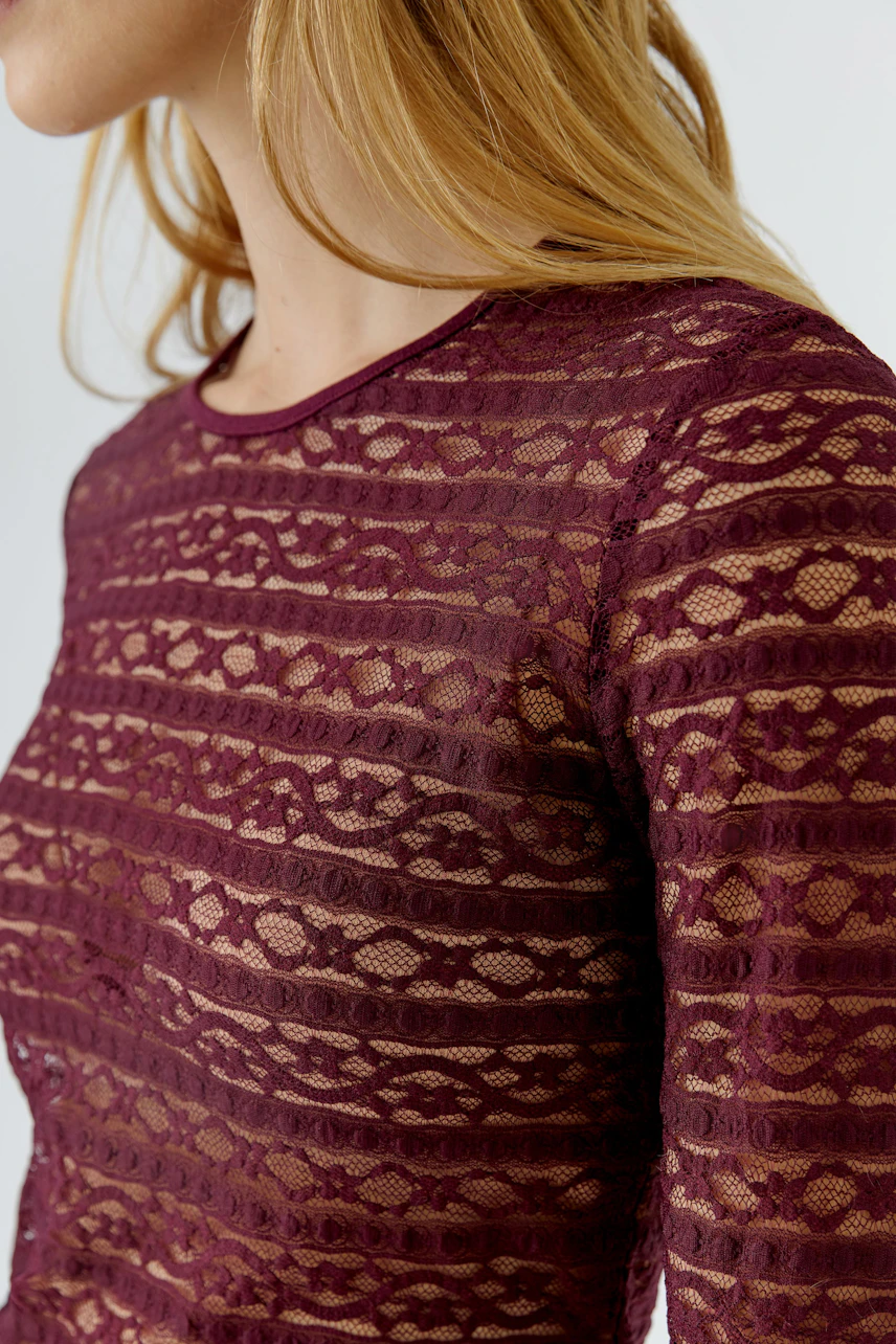 Frau im bordeauxroten Langarmshirt aus Spitze, seitlich fotografiert. Schlichtes Design, feminin und stilvoll.