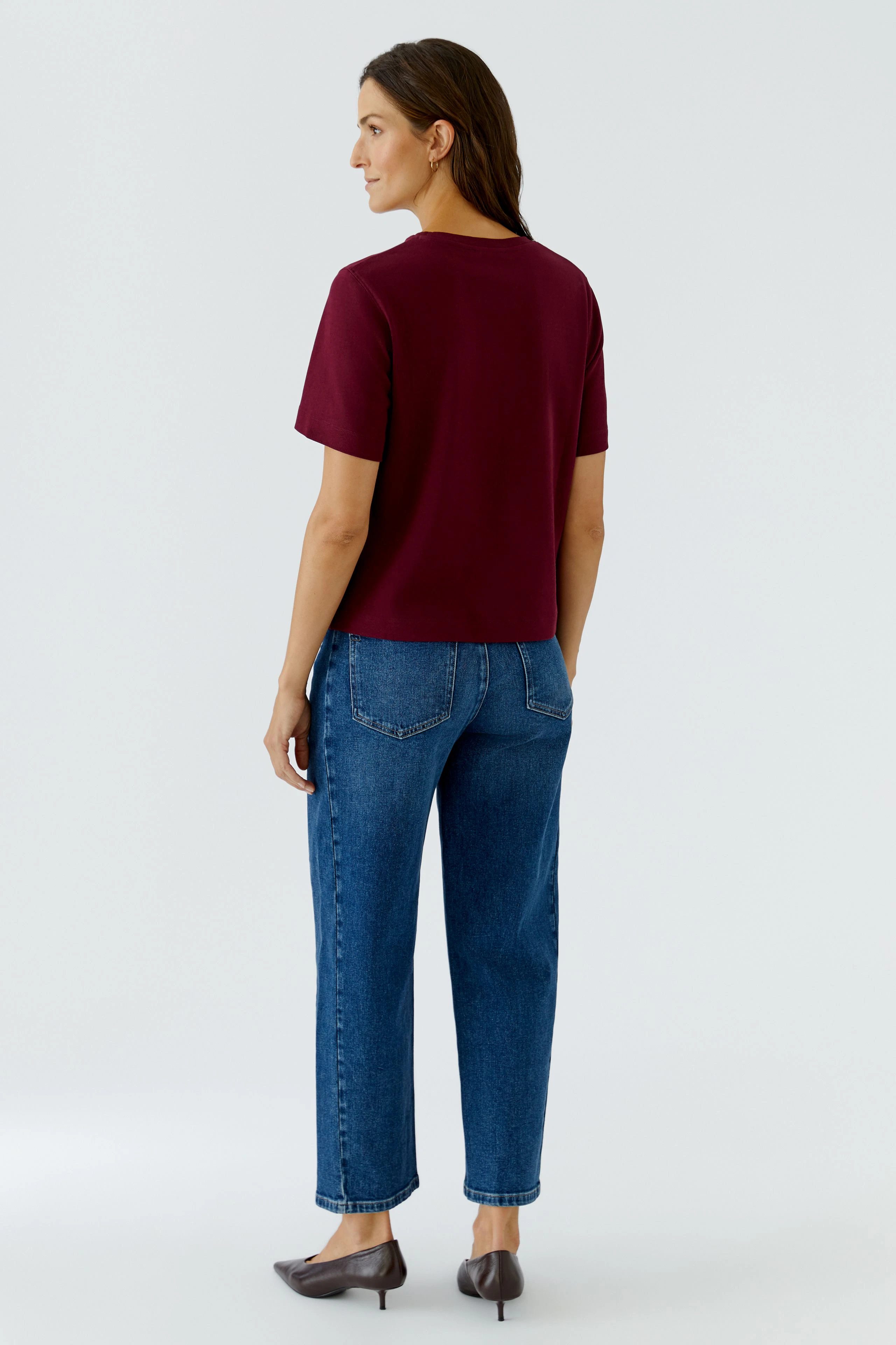 Casual women's T-shirt: Woman in a burgundy T-shirt and blue jeans, standing confidently.