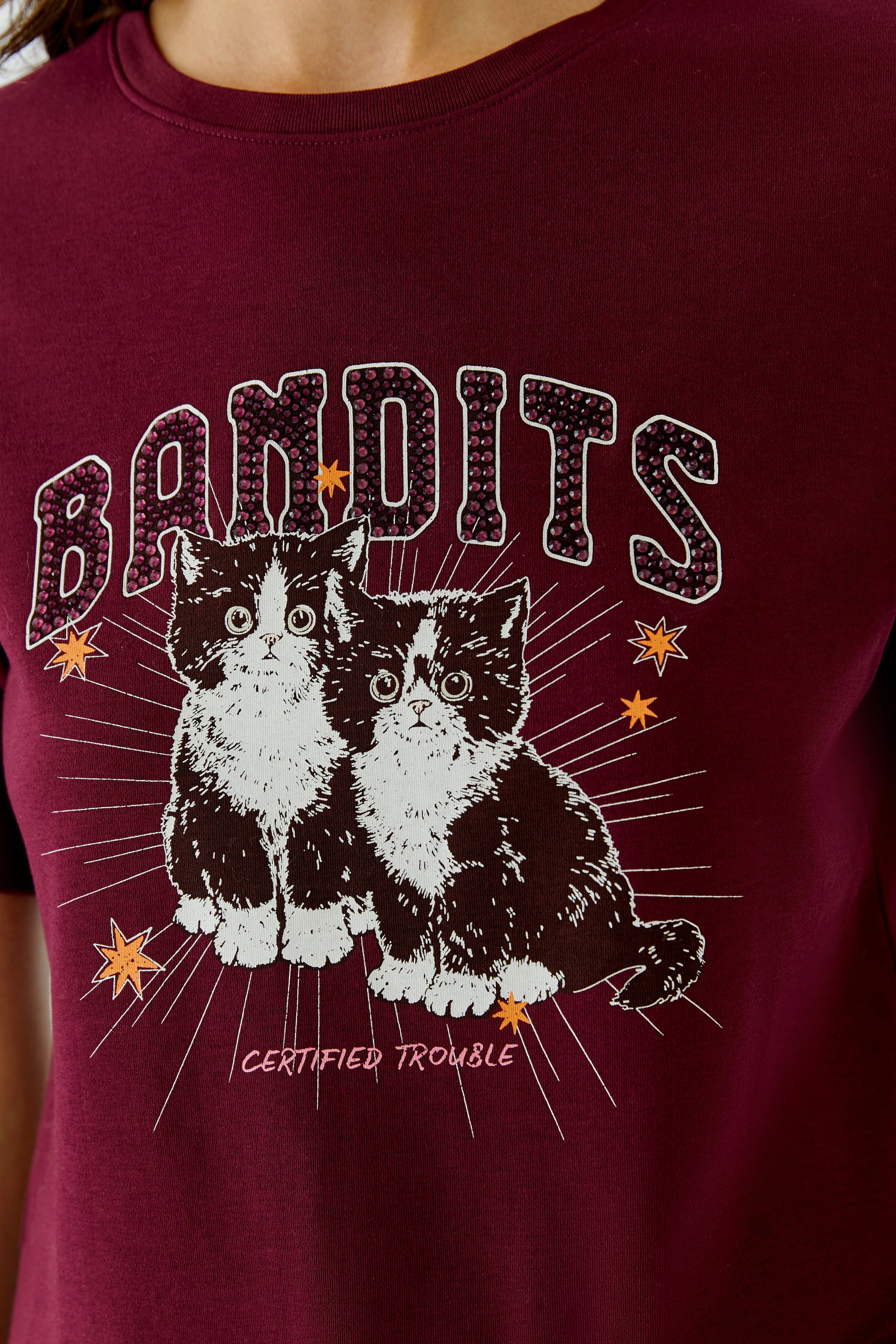 Women's T-shirt: Woman in a burgundy T-shirt with playful cat print and 'Bandits' text.