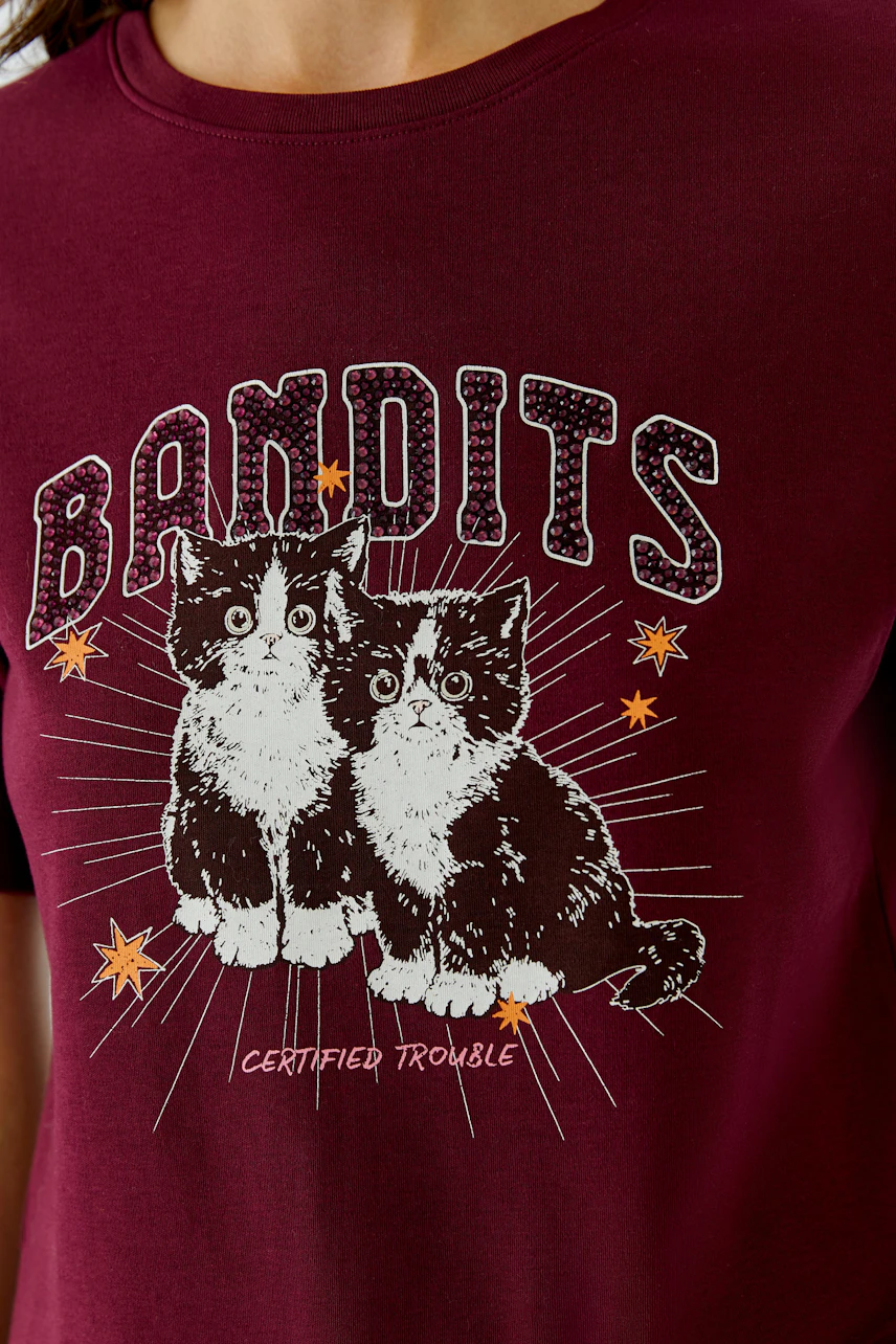 Damen-T-Shirt: Frau im weinroten T-Shirt mit Katzenmotiv und "Bandits"-Schriftzug.