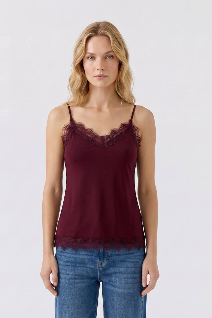 Damen-Top: Frau im weinroten Spitzentop mit schmalen Trägern und blauer Jeans, schlicht und stilvoll.