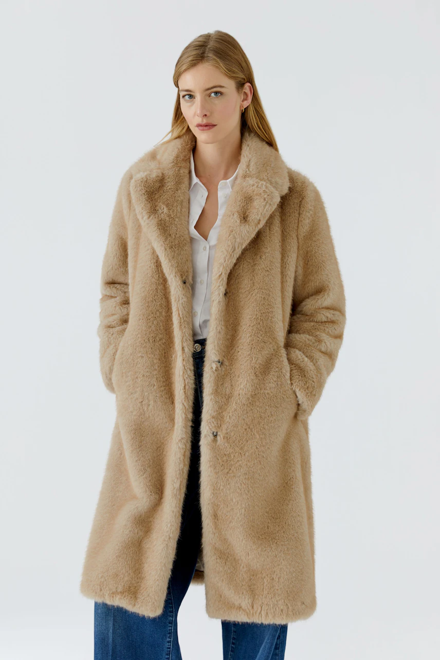 Cozy winter coat: Woman in a beige faux fur coat, white shirt, and jeans, exuding warmth and style.