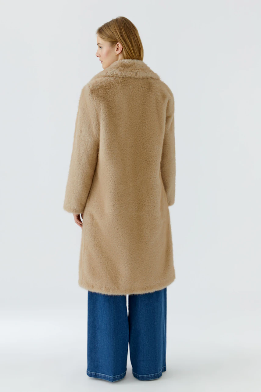 Casual winter coat: Woman in a cozy beige coat with wide jeans, viewed from the back.