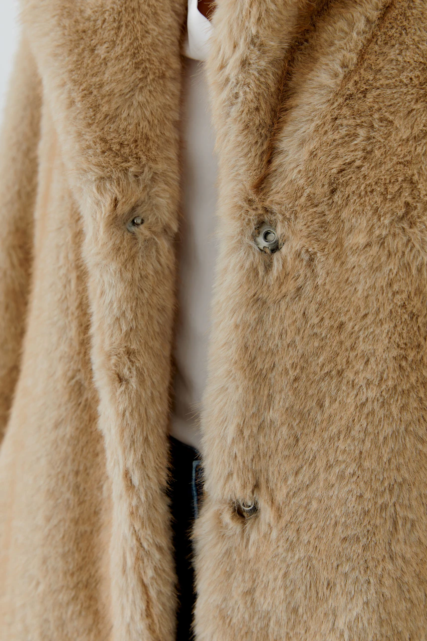 Cozy winter coat: Close-up of a fluffy beige coat with button details, perfect for cold weather.