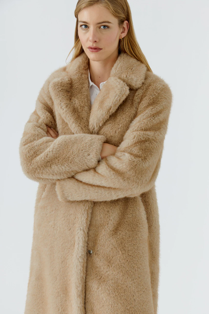 Cozy winter coat: Woman in a plush beige coat with a relaxed fit, arms crossed, exuding warmth.