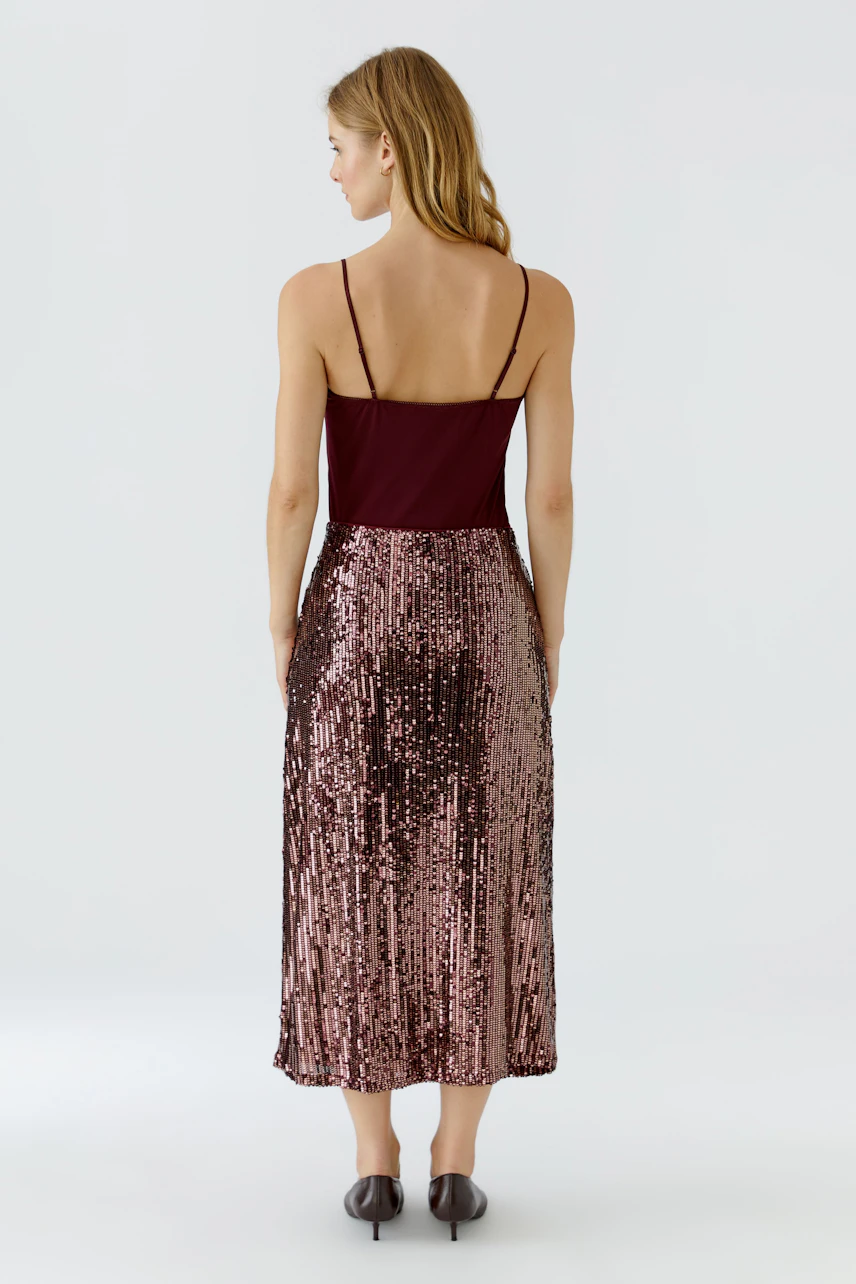 Woman in a sequin pencil skirt, burgundy top, and heels, viewed from the back.