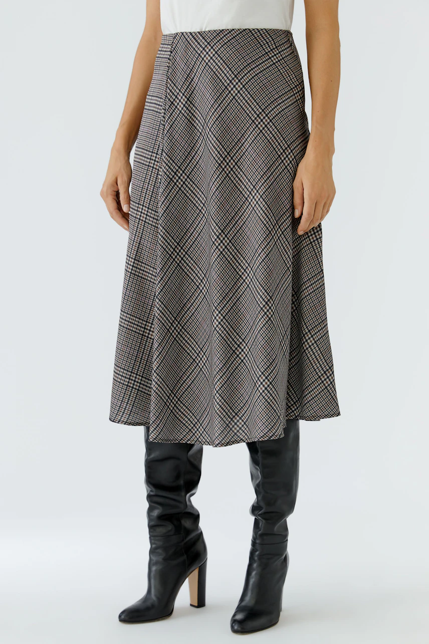 A-line skirt: Woman in a plaid A-line skirt with a white top and black boots.