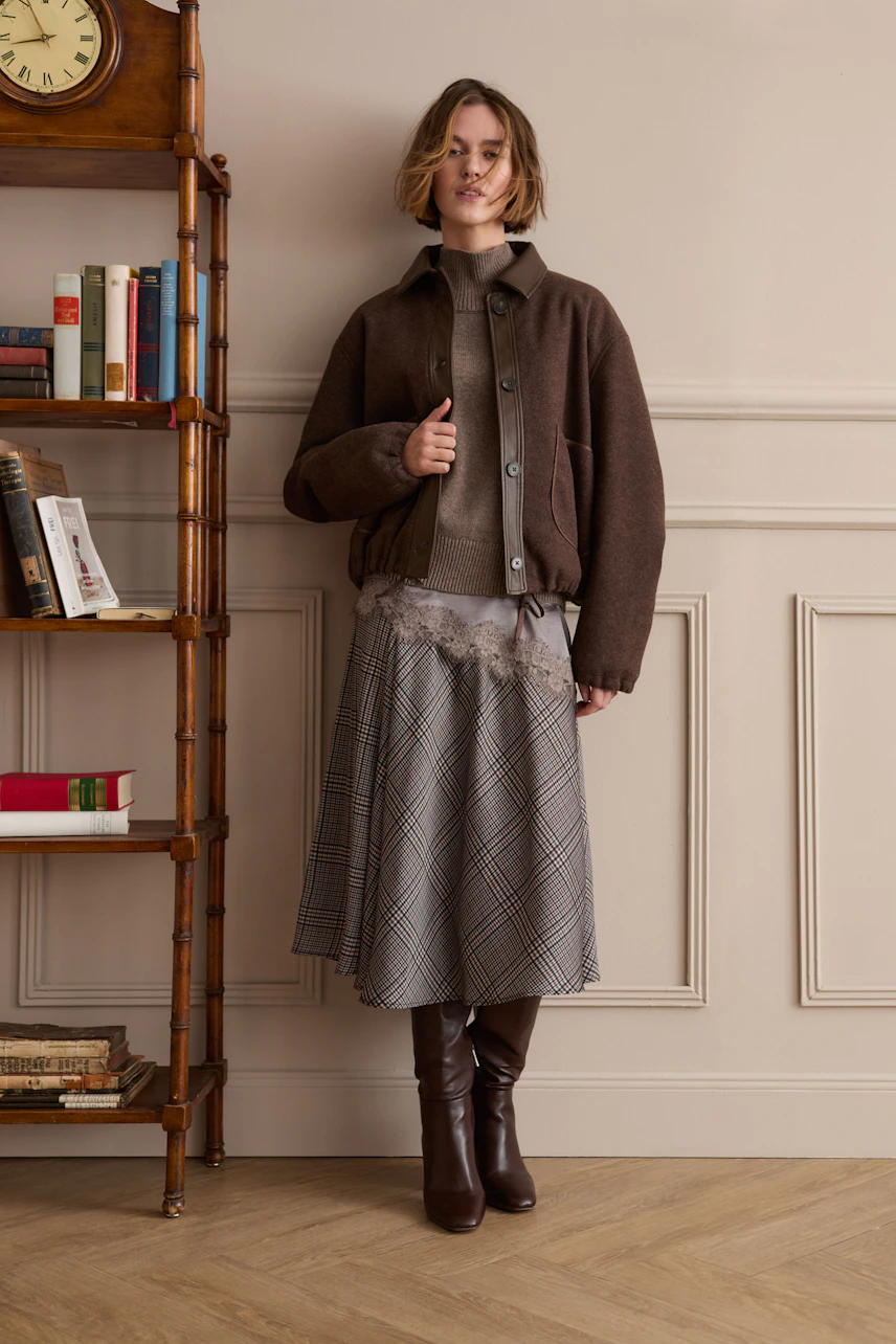 A-line skirt: Woman in a plaid A-line skirt, brown jacket, and boots stands confidently.