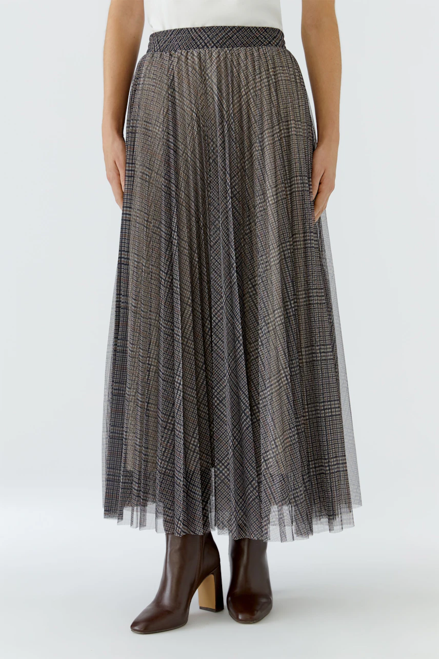 Woman in a plaid pleated skirt, white top, and brown boots. The skirt flows gracefully to the ankles.