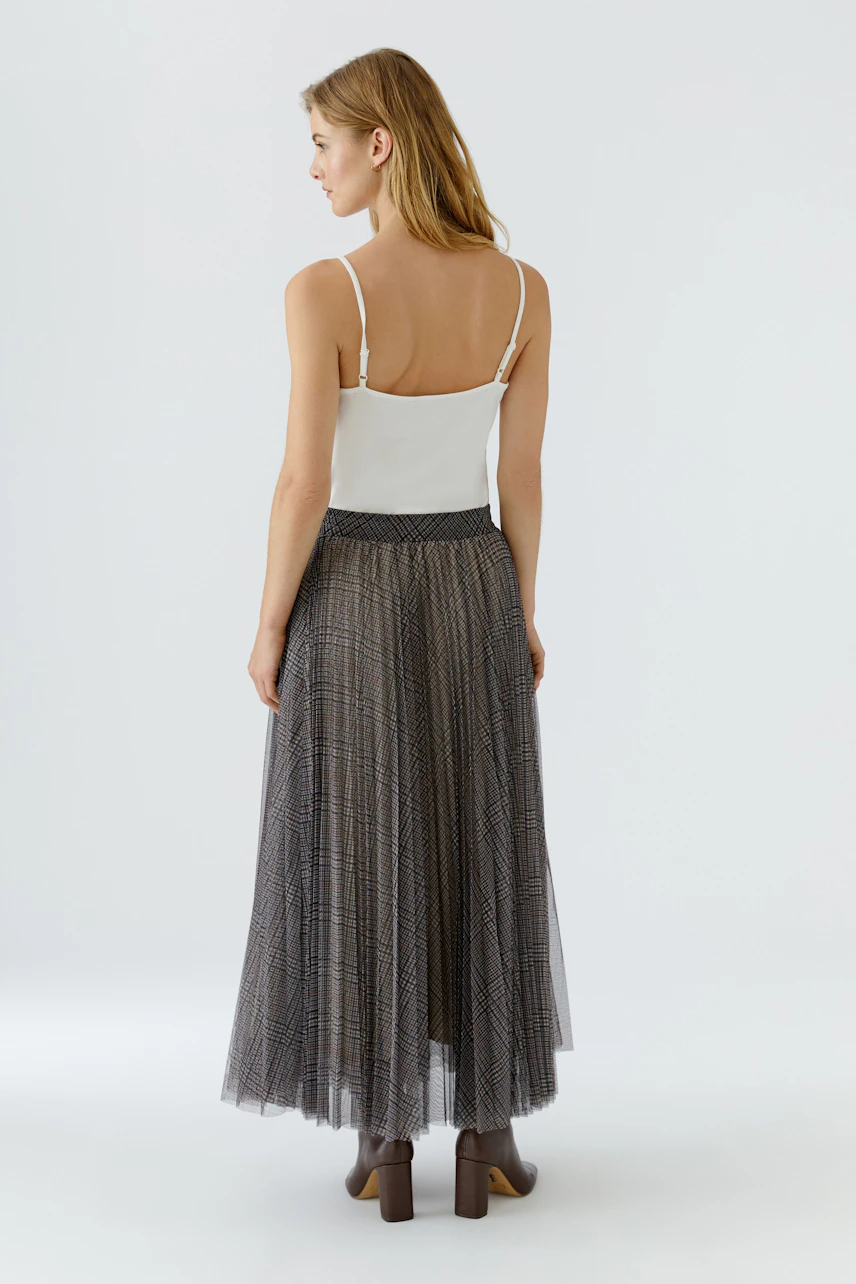 Woman in a pleated skirt and white top, viewed from the back, showcasing the skirt's flowy design.