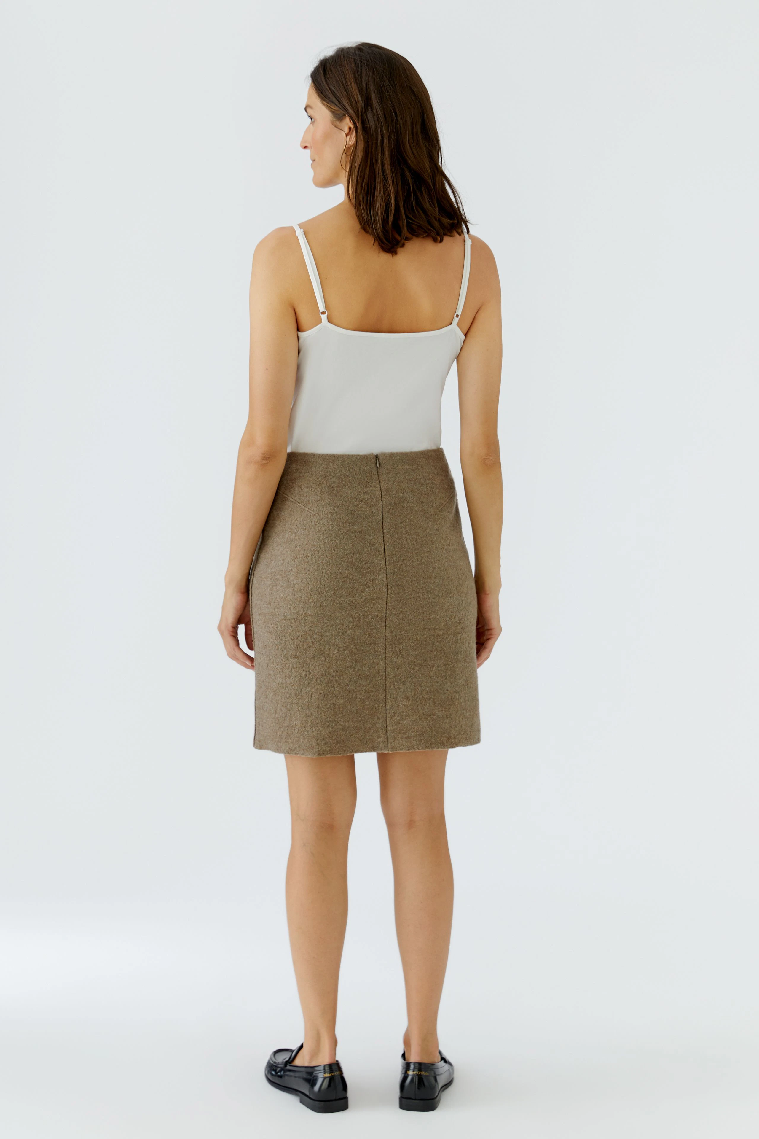 Woman in A-line skirt and white top, standing confidently. Simple, casual style with black shoes.