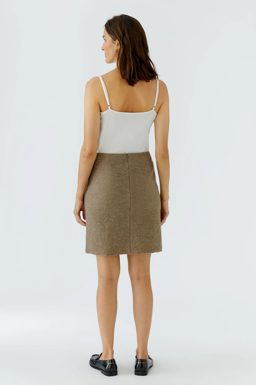 Woman in A-line skirt and white top, standing confidently. Simple, casual style with black shoes.