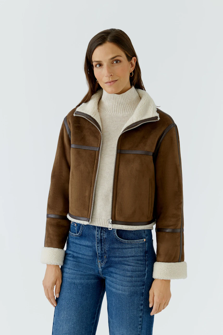 Lederimitatjacke: Frau in brauner Jacke mit hellem Kragen und Jeans, lässiger Look.