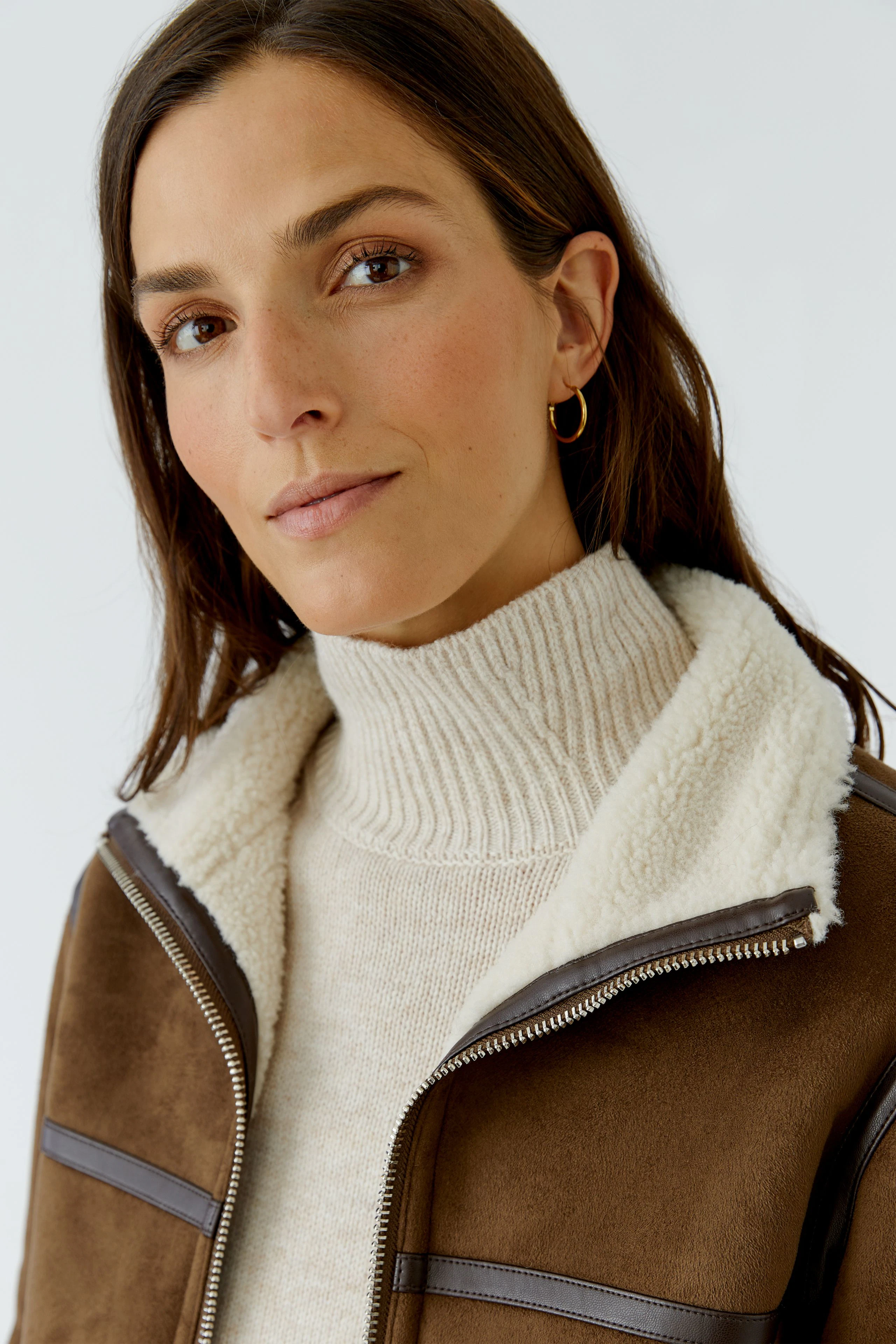 Woman in faux leather jacket with shearling collar, wearing a cream turtleneck pullover, looking confident.