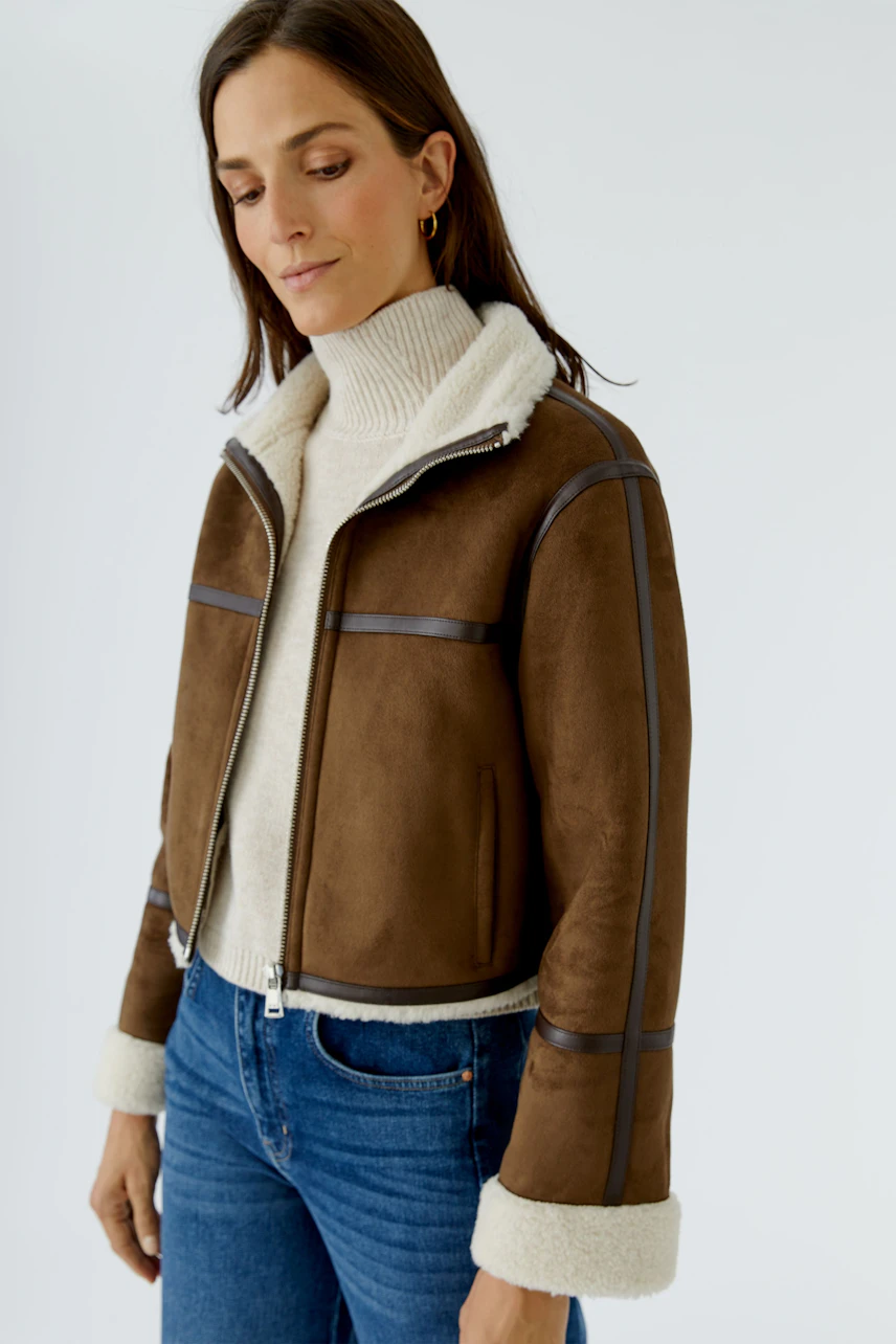 Lederimitatjacke: Frau in brauner Jacke mit weißem Kragen und Jeans, lässiger Look.