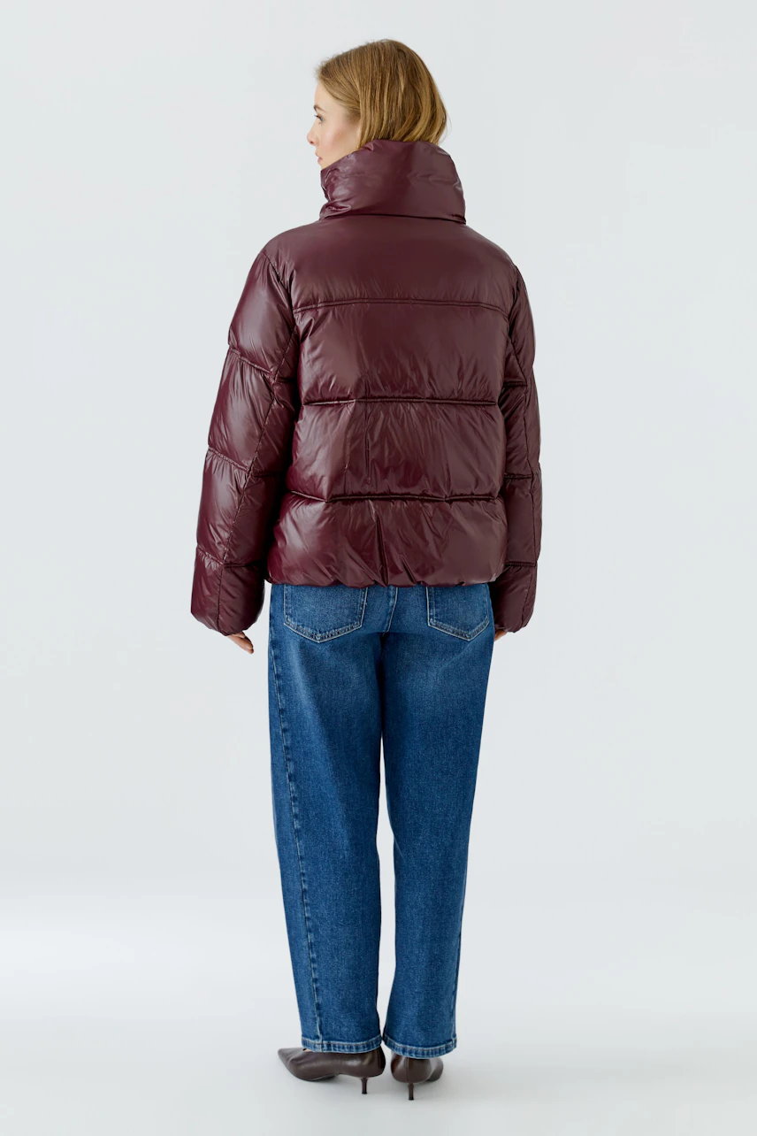 Frau in bordeauxfarbener Outdoorjacke, lässig kombiniert mit blauen Jeans, von hinten gezeigt.