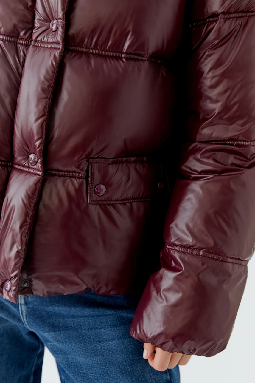 Bordeauxrote Outdoorjacke: Detailansicht der Jacke mit Knöpfen, kombiniert mit blauer Jeans.