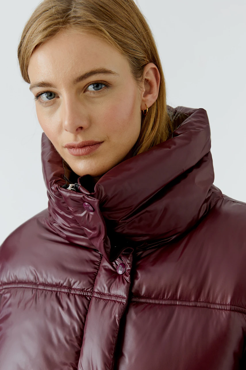Frau in bordeauxfarbener Outdoorjacke mit hohem Kragen, blickt direkt in die Kamera.