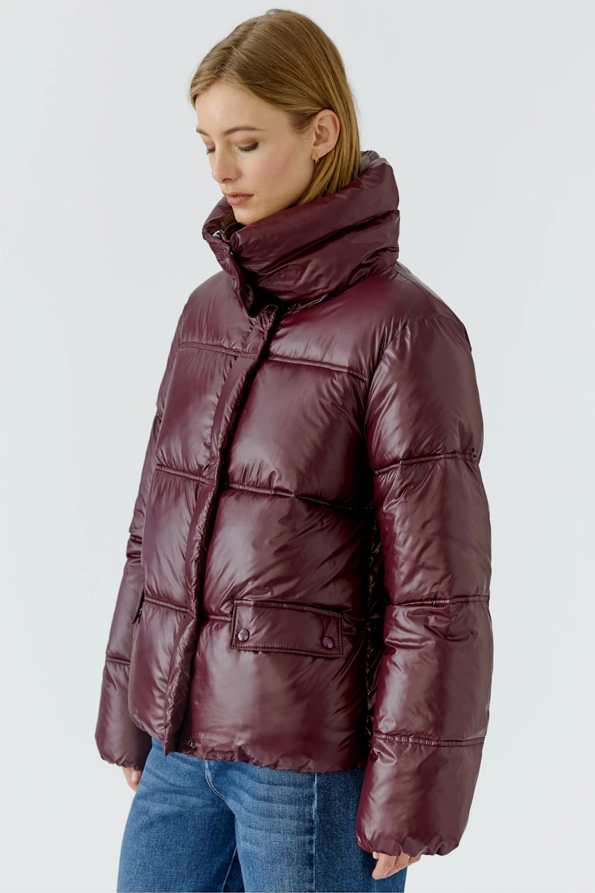 Frau in bordeauxfarbener Outdoorjacke, warm gefüttert, mit hohem Kragen, kombiniert mit blauen Jeans.