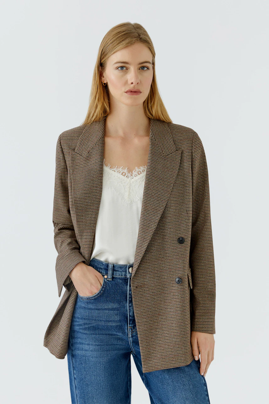 Casual blazer: Woman in a checked blazer over a white top and jeans, hands in pockets, looking confident.