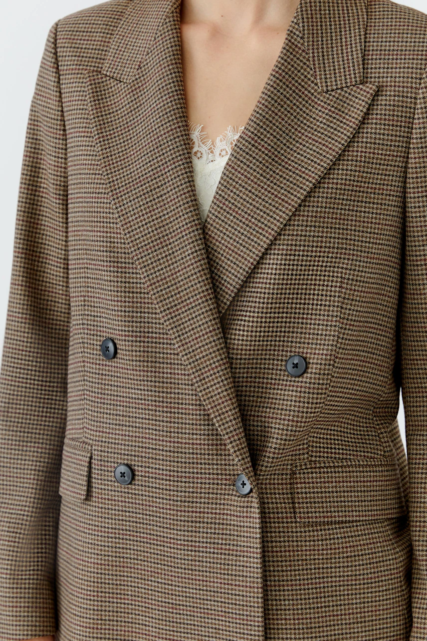 Women's blazer: Woman in a brown checkered blazer with a subtle lace top underneath.