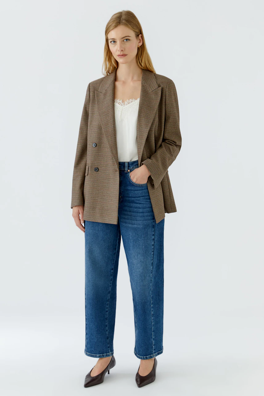 Casual blazer: Woman in a brown checkered blazer, white top, and blue jeans, standing confidently.