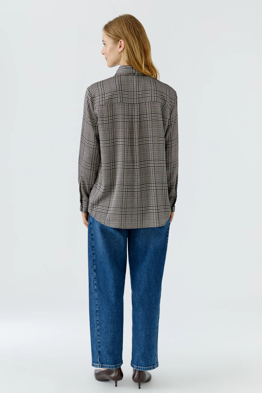 Woman in a plaid pussy-bow blouse and blue jeans, viewed from the back.