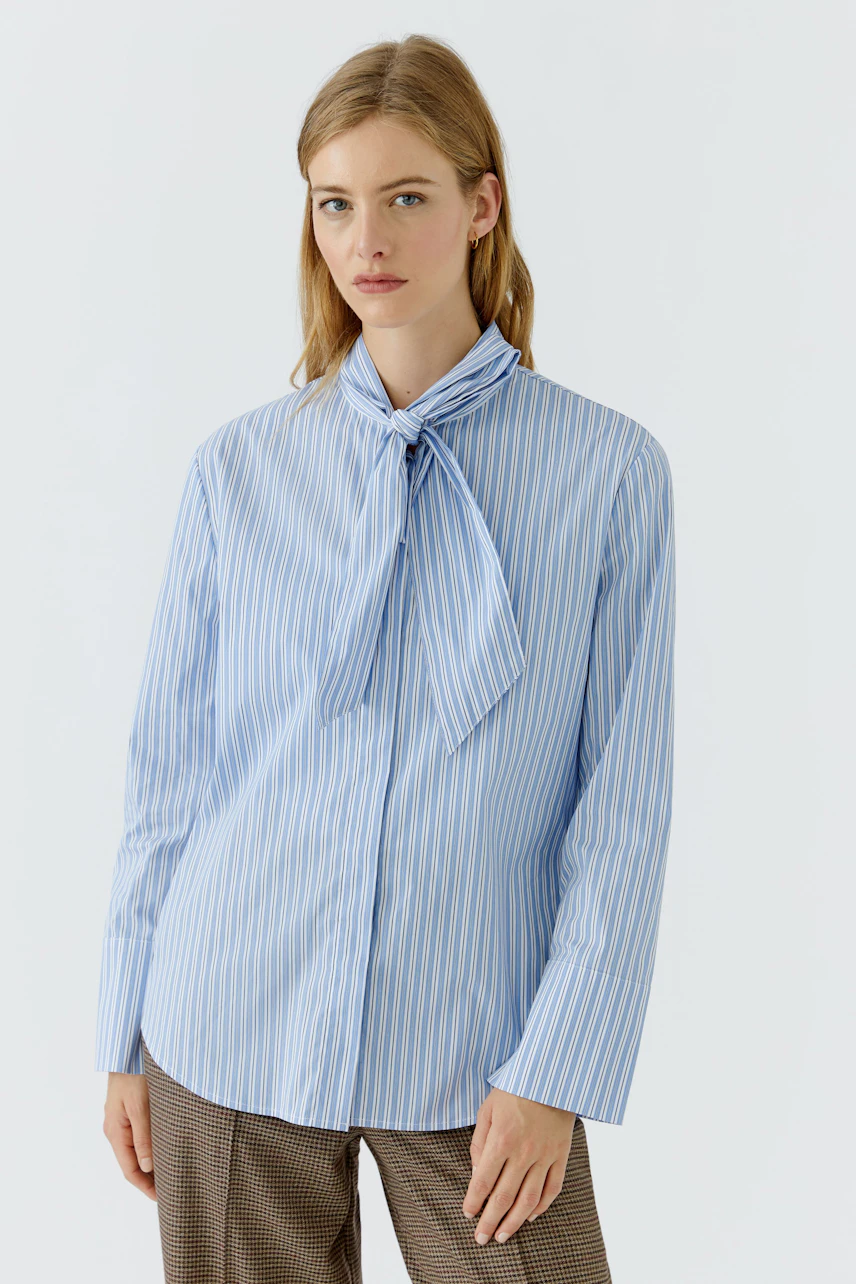 Striped pussy-bow blouse: Woman in a blue and white striped blouse with a bow tie, looking poised.