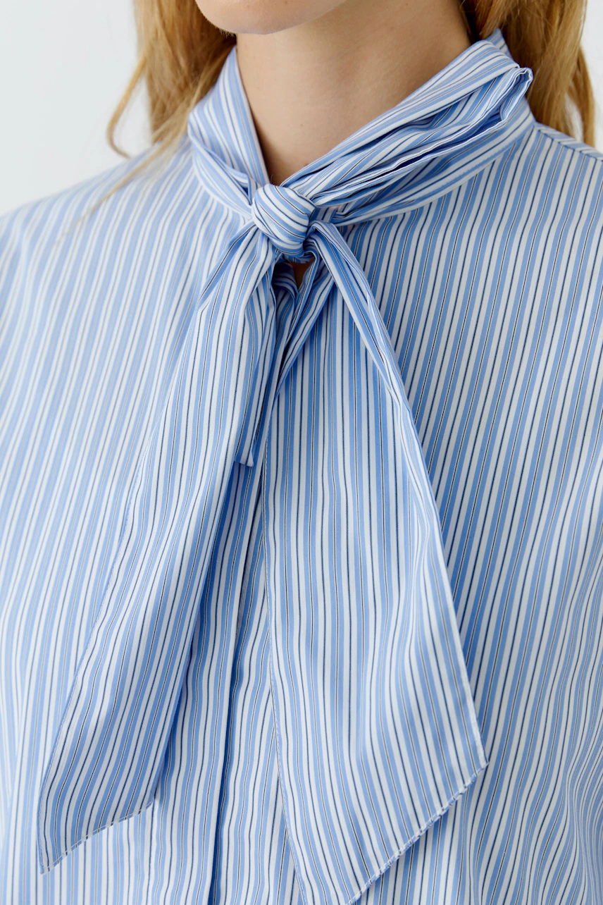 Striped pussy-bow blouse: Woman in blue and white striped blouse with a tied bow at the neck.