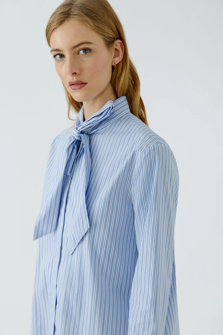 Striped pussy-bow blouse: Woman in a blue and white striped blouse with a bow tie, looking confidently.