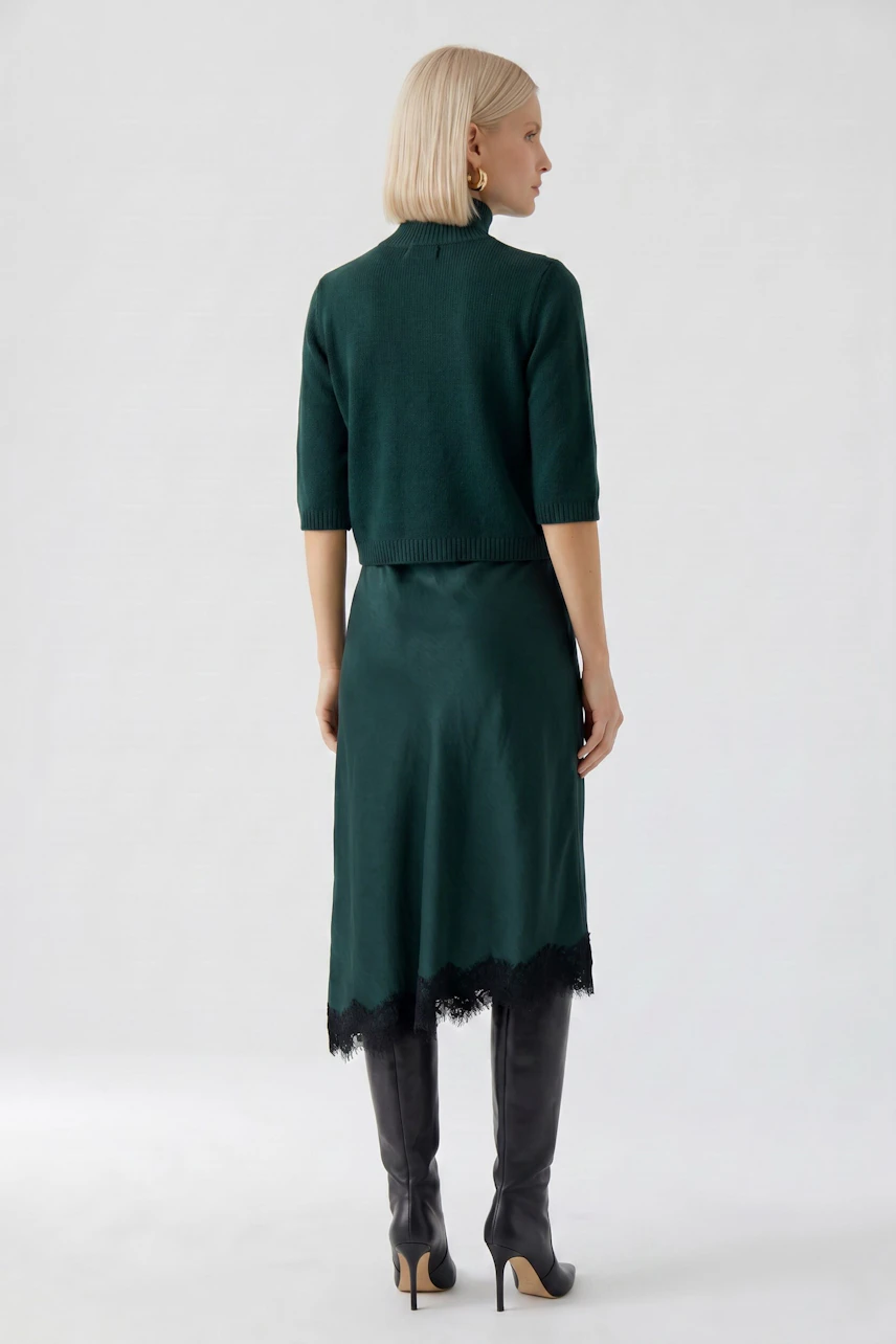 Woman in green pencil skirt with lace hem, paired with matching top and black knee-high boots.