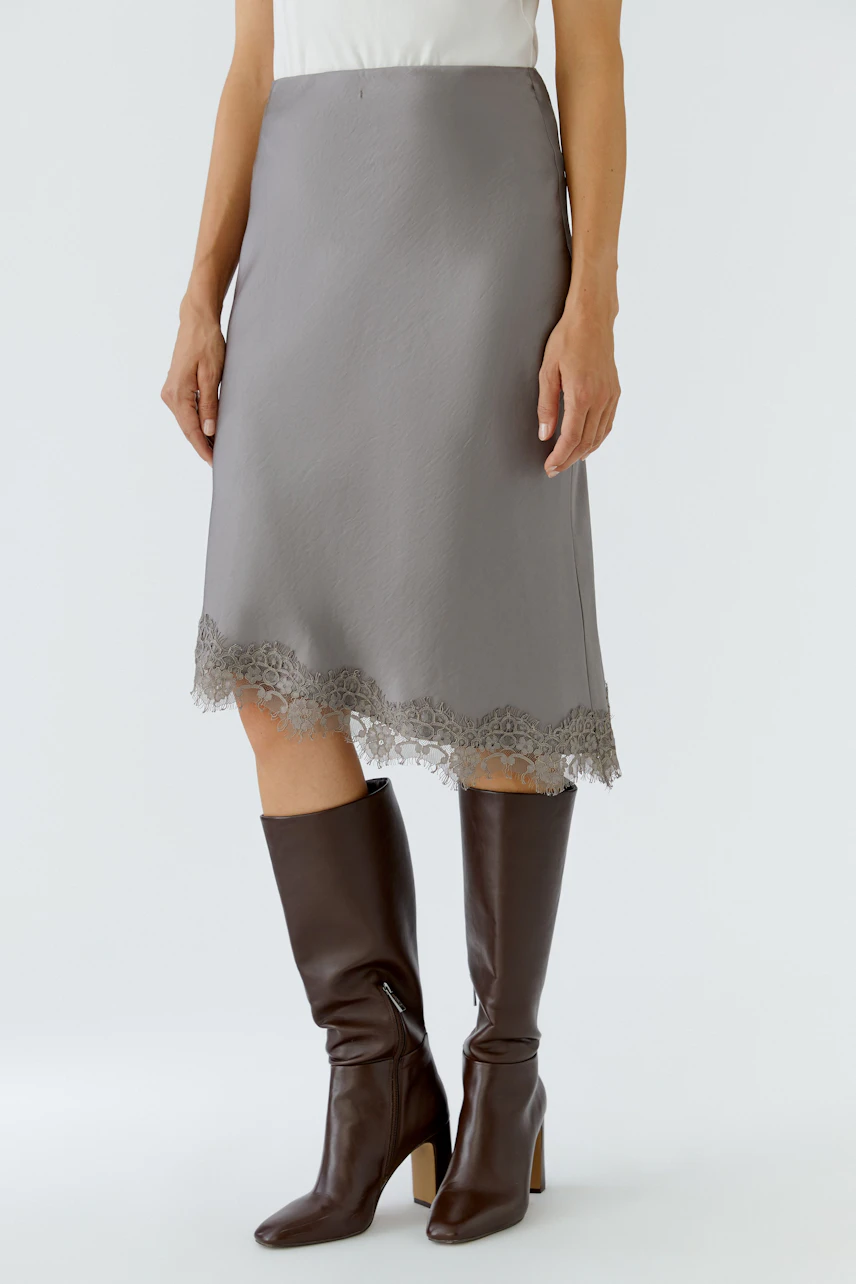 Woman in a grey pencil skirt with lace hem, paired with tall brown boots.