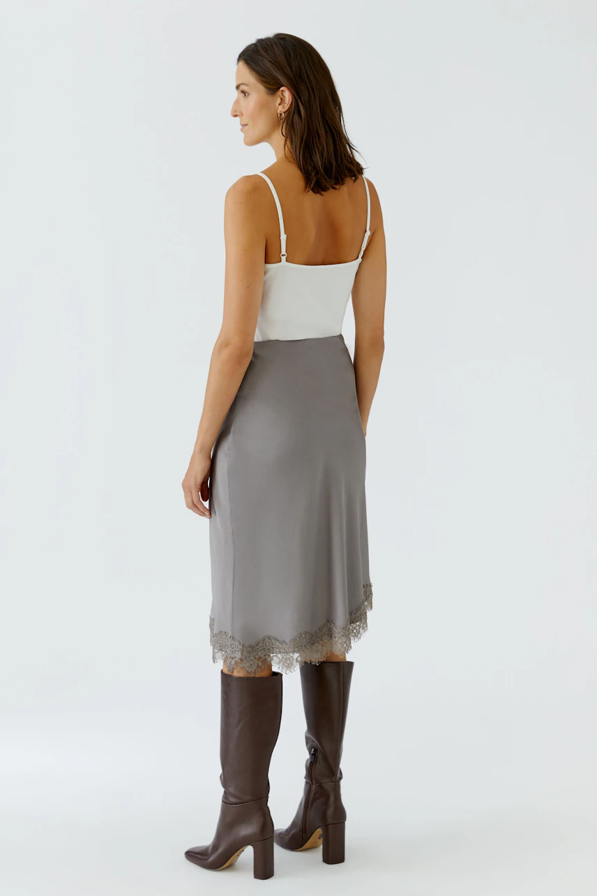 Woman in a sleek pencil skirt with lace hem, paired with a white top and tall brown boots.