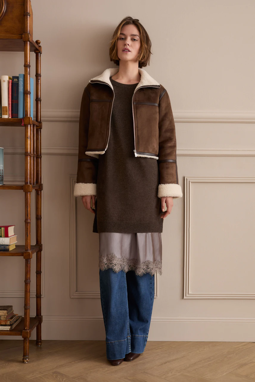 Woman in layered outfit: brown jacket, long top, and jeans. Focus on the pencil skirt underneath.